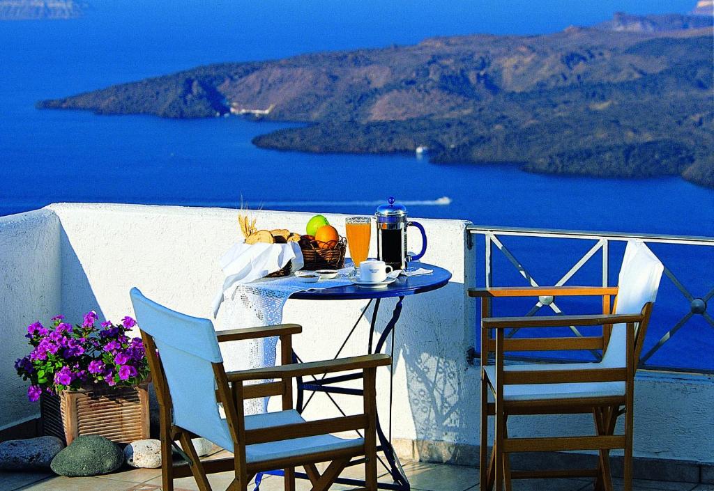 una mesa y sillas en un balcón con vistas al océano en Theoxenia Caldera Hotel en Fira