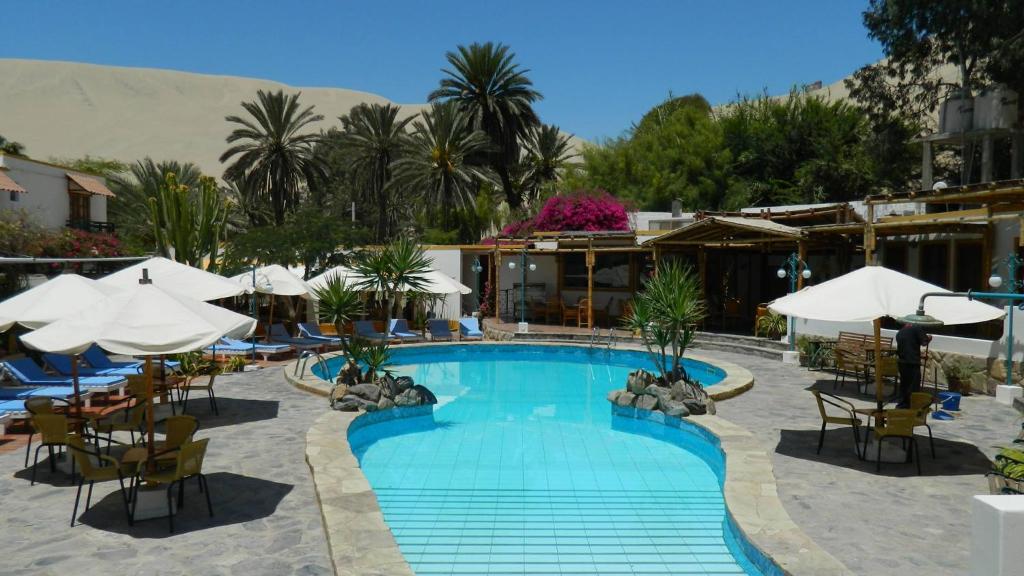 una piscina con sillas y sombrillas en un hotel en Hosteria Suiza, en Ica