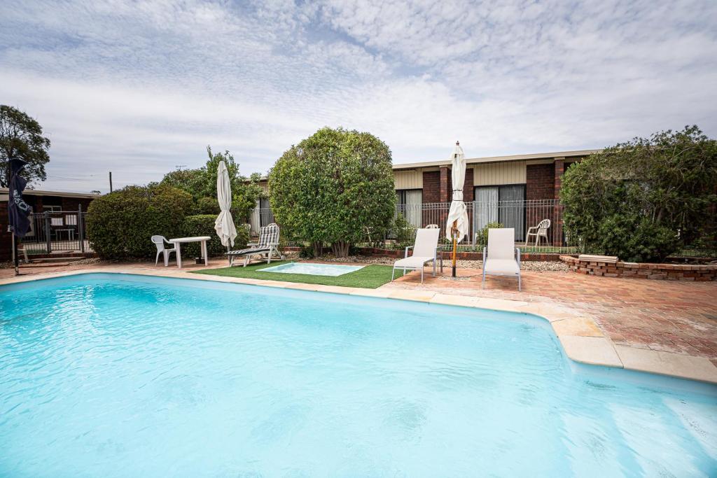 a large swimming pool with two chairs and a table at Riviana Motel in Deniliquin