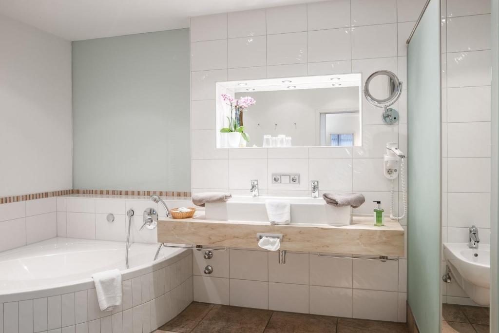 a white bathroom with a tub and a sink at Landhotel Böld Oberammergau in Oberammergau