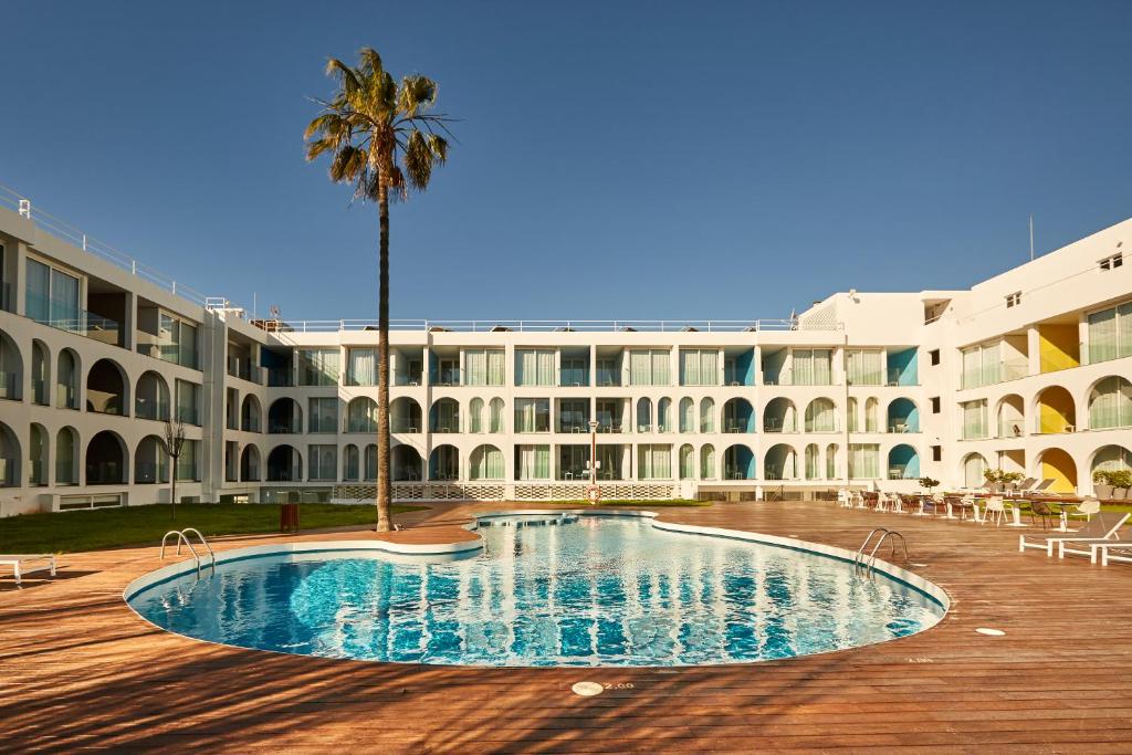 un grand bâtiment avec un palmier et une piscine dans l'établissement Ebano Hotel Apartments & Spa, à Playa d'en Bossa