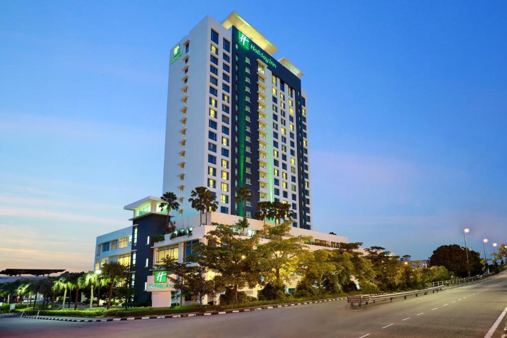 a tall building with palm trees in front of a street at Holiday Inn Melaka, an IHG Hotel in Melaka