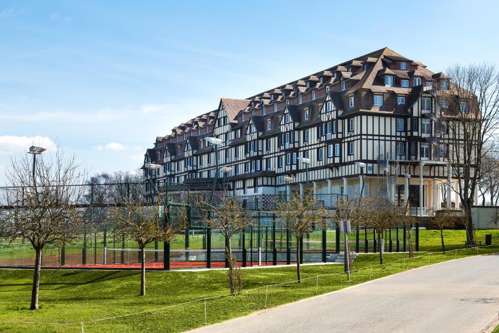 ein großes Gebäude in einem Park mit Bäumen davor in der Unterkunft Hôtel Barrière L'Hôtel du Golf in Deauville