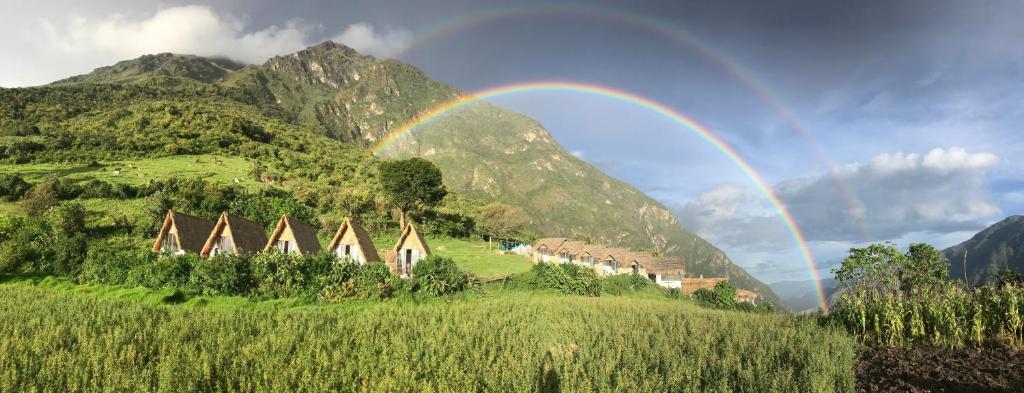 een regenboog over een groep huizen op een heuvel bij Choquequirao Sanctuary Lodge in Cuzco