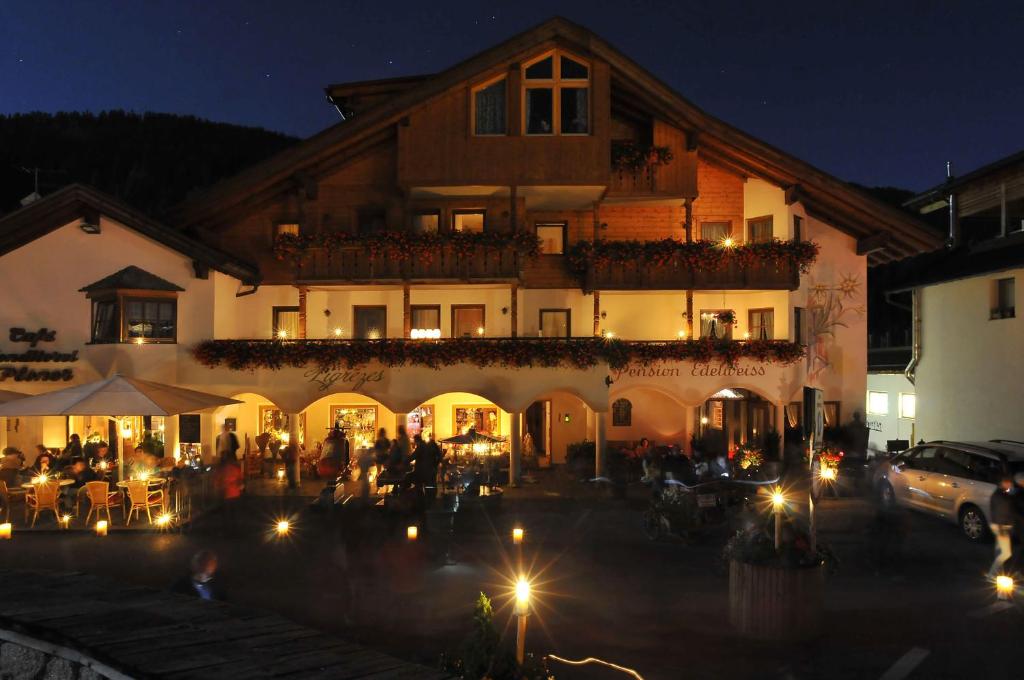 a building with people sitting outside of it at night at Pensione Edelweiss in San Cassiano