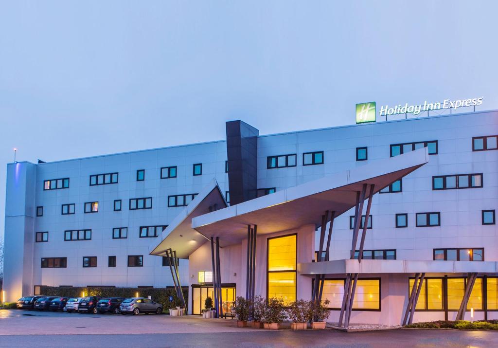 un gran edificio blanco con coches aparcados en un aparcamiento en Holiday Inn Express Milan-Malpensa Airport, an IHG Hotel, en Case Nuove