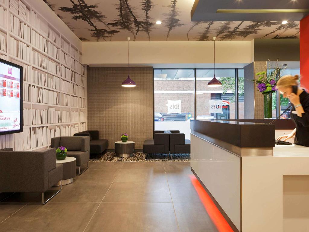 a woman standing at a counter in a waiting room at ibis London Shepherds Bush - Hammersmith in London