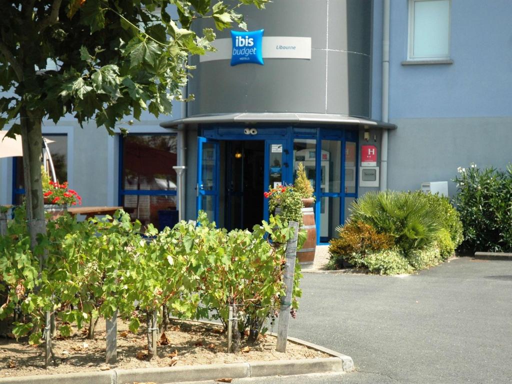 un bâtiment de bureau avec une porte bleue et quelques buissons dans l'établissement ibis budget Libourne, à Libourne