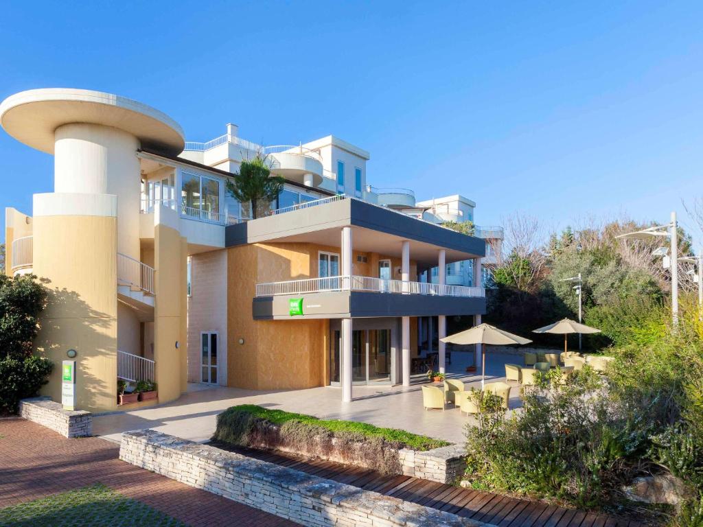 a large building with a balcony with tables and umbrellas at Ibis Styles Bari Giovinazzo in Giovinazzo