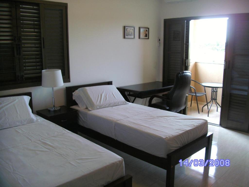 a hotel room with two beds and a table and a desk at Pousada Jaó in Goiânia