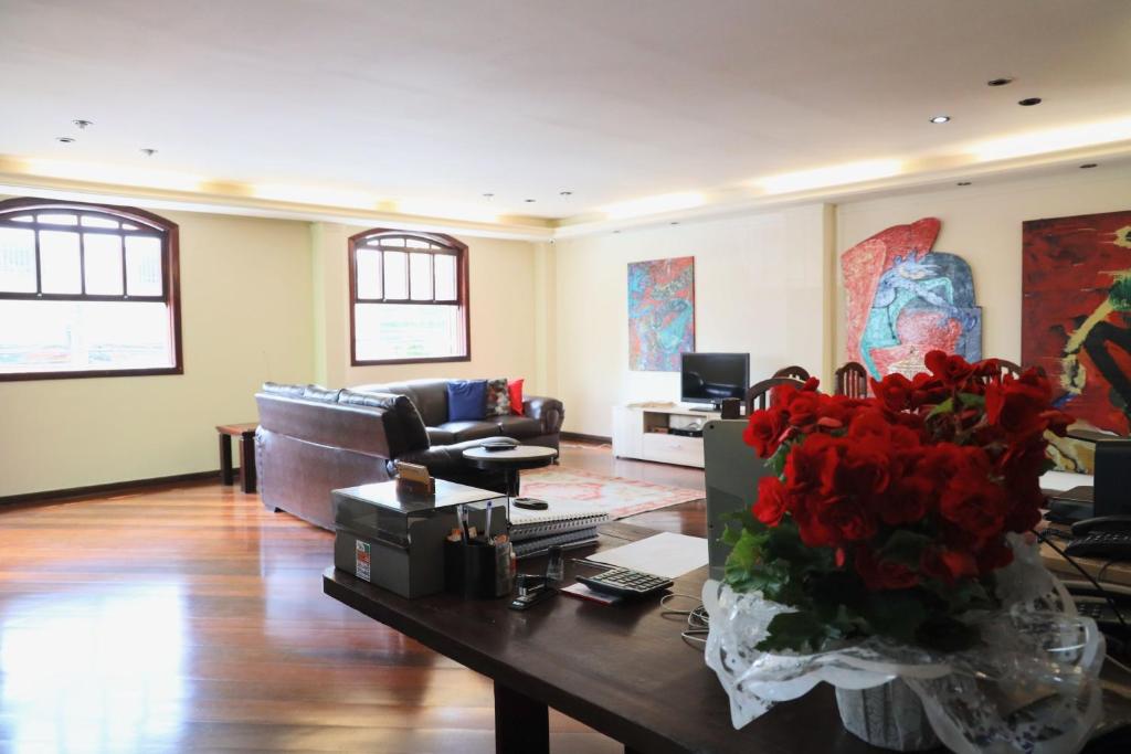 a living room with a couch and a table with red flowers at Pousada Anexo in Niterói