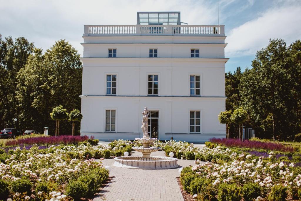 un edificio blanco con una fuente en medio de un jardín en Vila Komoda en Palanga