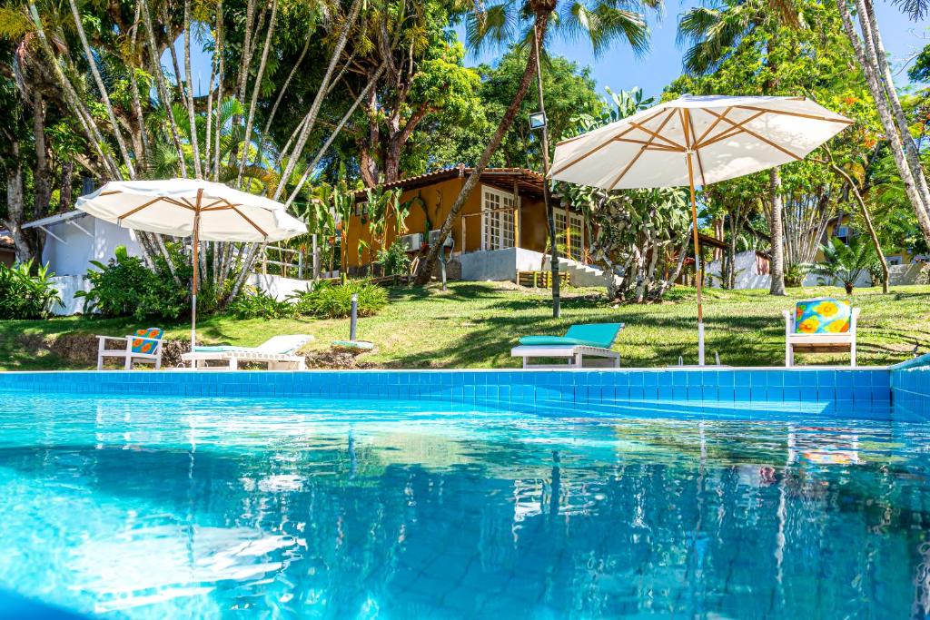 una piscina con 2 sombrillas y una casa en Pousada Rio da Vila, en Porto Seguro