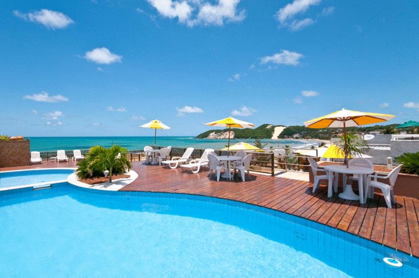 uma piscina com mesas, cadeiras e guarda-sóis em Mirador Praia Hotel em Natal