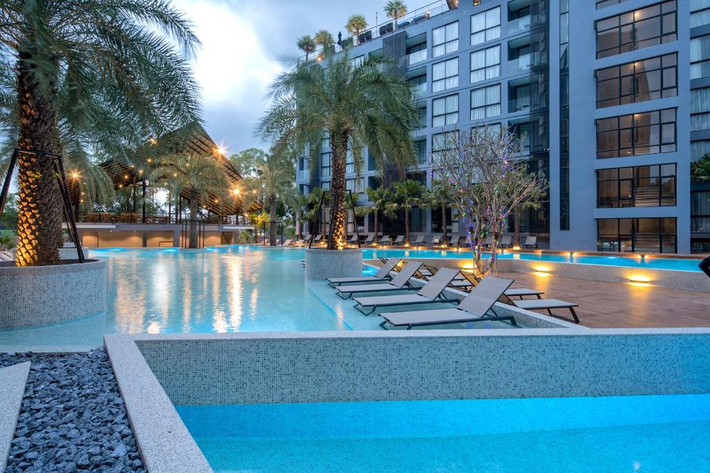 Citygate Kamala Resort and Residence في شاطئ كامالا: مسبح بكراسي الصالة والنخيل والمباني