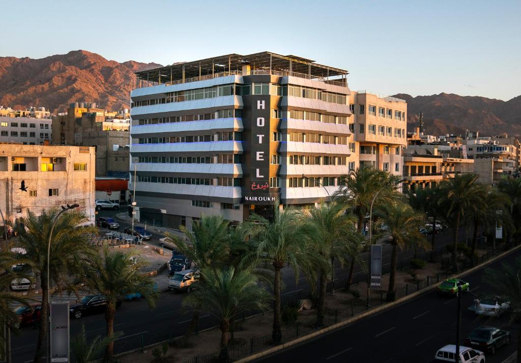 a tall building with palm trees in a city at Nairoukh Hotel Aqaba in Aqaba