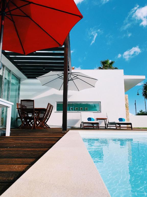 a patio with a red umbrella and a swimming pool at Villa Mar Garajau in Caniço
