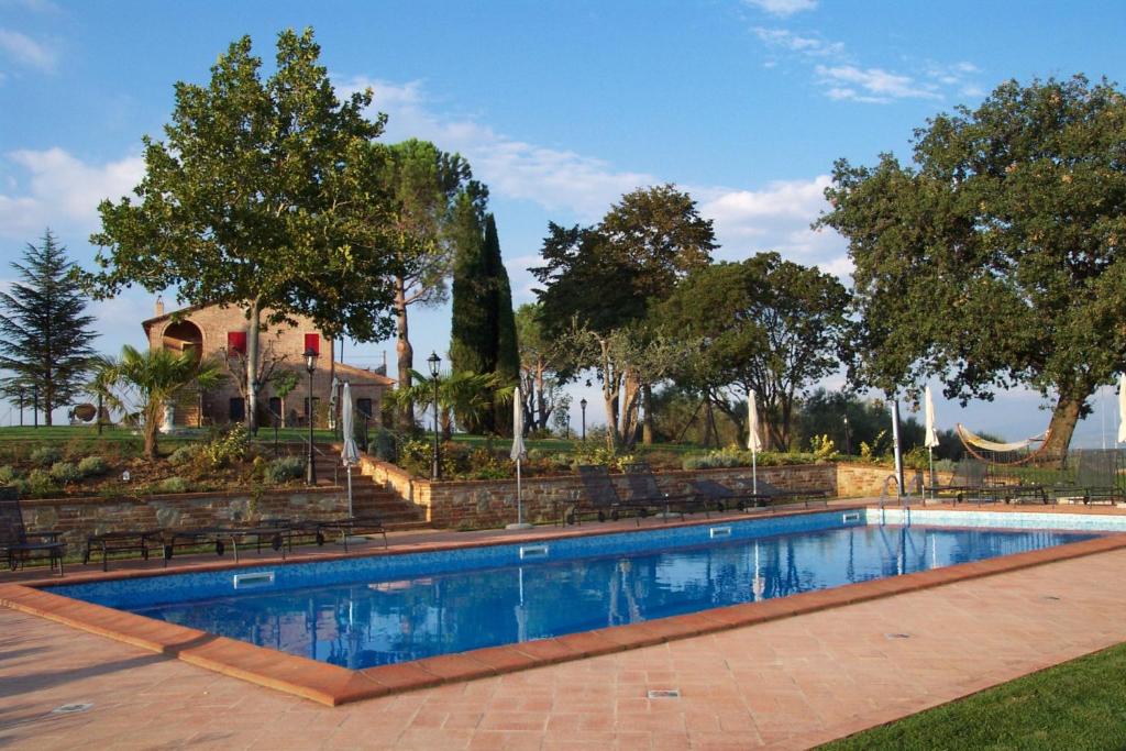 a swimming pool with benches and trees and a house at Podere Fontegallo in Castiglione del Lago