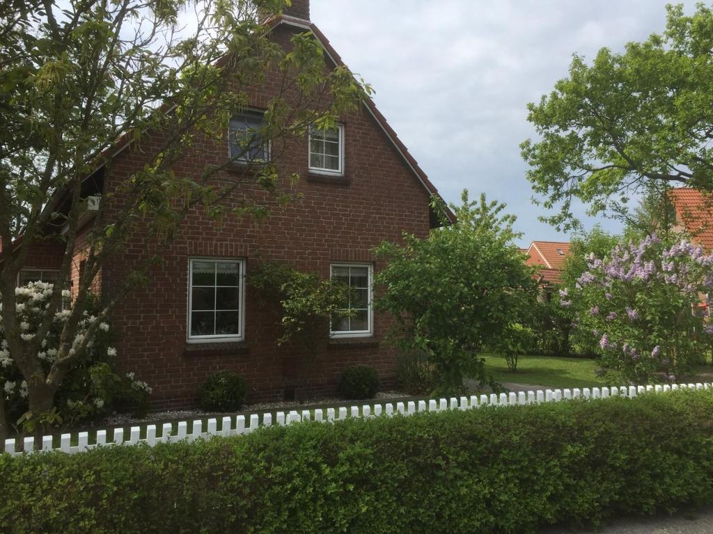 uma casa de tijolos vermelhos com uma cerca branca em Ferienhaus Schonerweg 9 in Norddeich em Norddeich