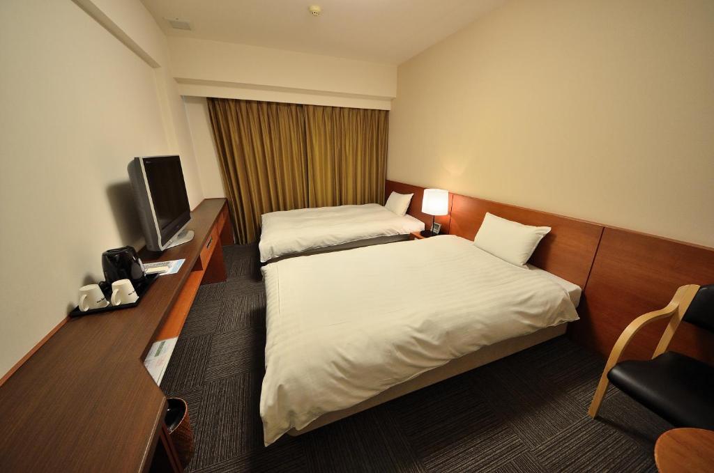 a hotel room with two beds and a television at Dormy Inn Hirosaki in Hirosaki