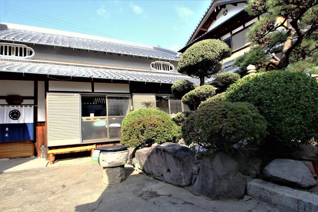 貝塚市的住宿－ゲストハウス喜平，一座有灌木丛和前方石墙的房子