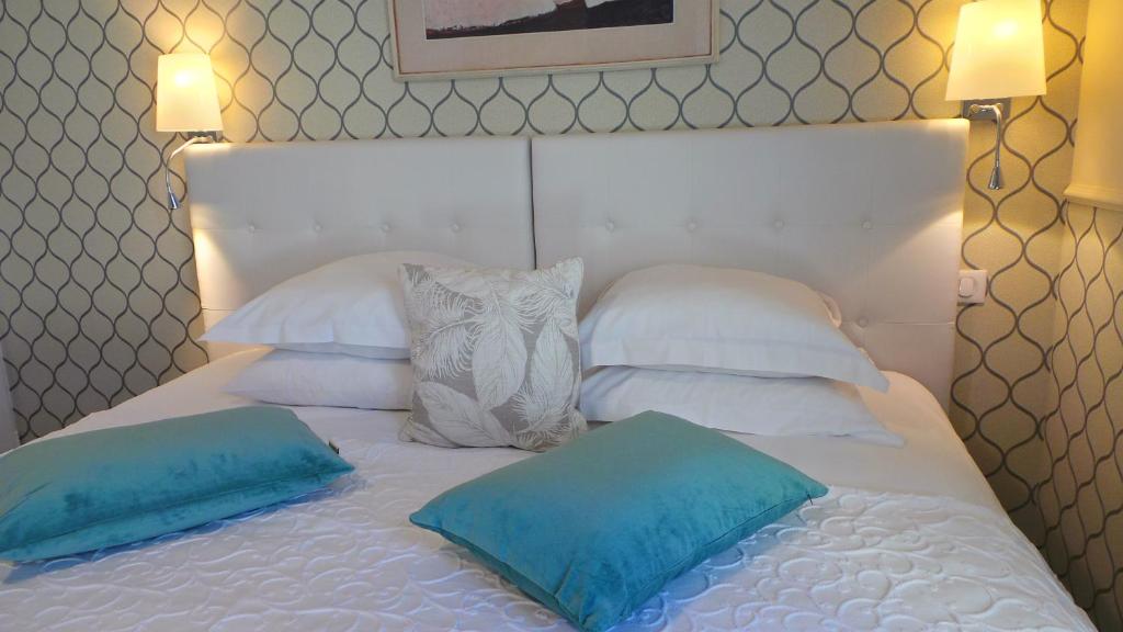 a white bed with two blue pillows on it at Hotel Relais Du Postillon in Antibes