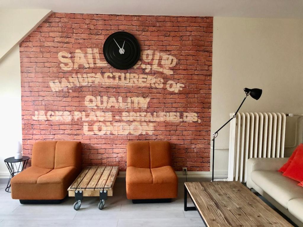 2 chaises et une horloge sur un mur de briques dans l'établissement Gîte Le Vintage Mulhouse, à Mulhouse