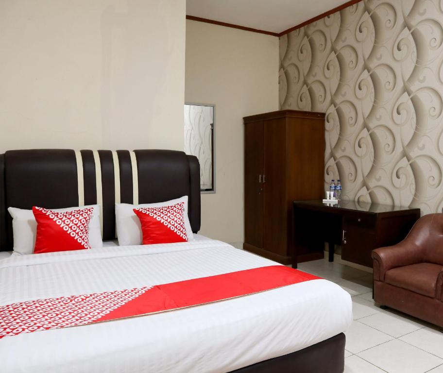 a bedroom with a bed with red pillows and a chair at OYO 1686 Lenggogeni House in Padang