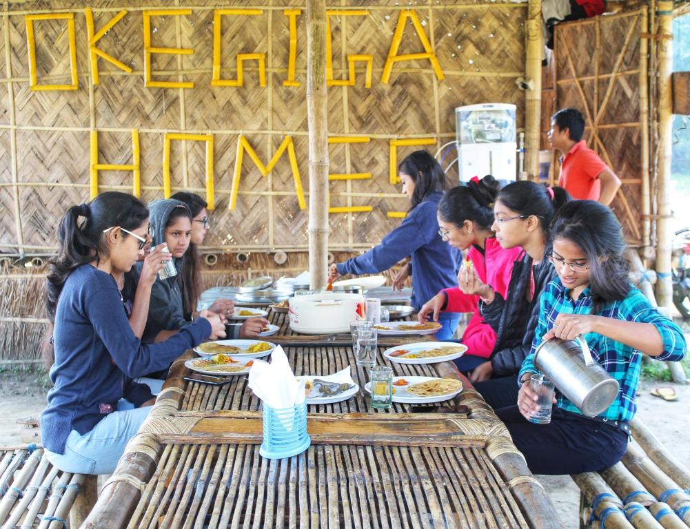 a group of people sitting around a table eating food at Okegiga Homes in Majuli