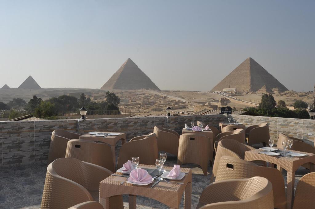 TuT Pyramids View في القاهرة: مطعم فيه كراسي وطاولات مع الاهرامات في الخلف