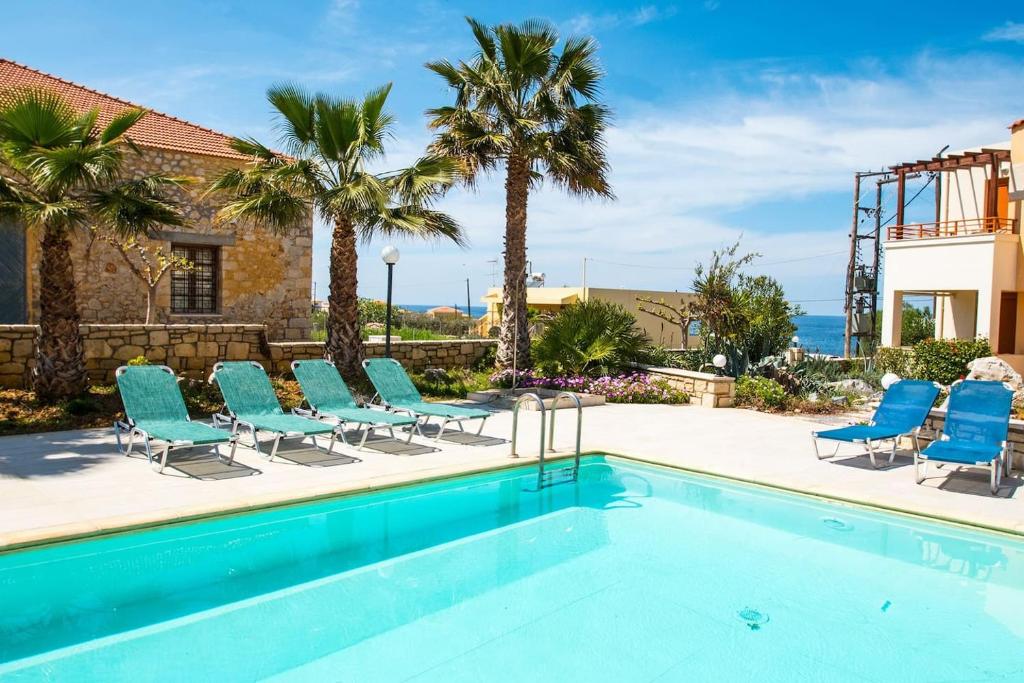 una piscina con sillas azules y palmeras en Sea La Vie house, close to the beach, By ThinkVilla, en Panormos Rethymno