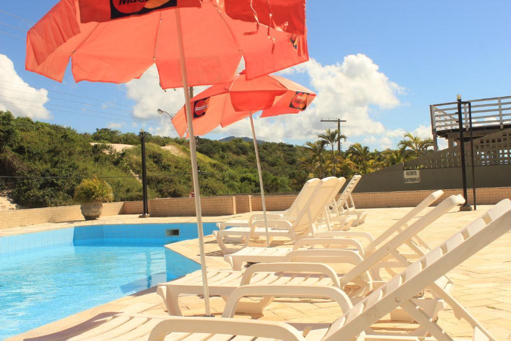 un grupo de sillas y sombrillas junto a una piscina en Pousada das Dunas Via Praia Apart Hotel, en Florianópolis