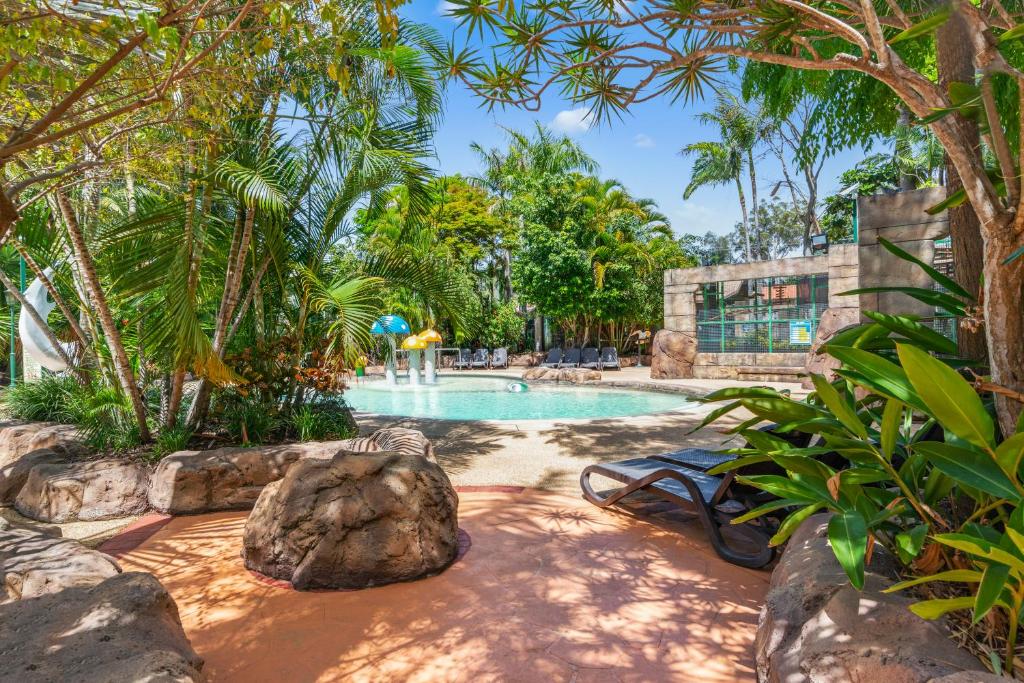 ein Pool in einem Resort mit Bäumen und einem Felsen in der Unterkunft Ashmore Palms Holiday Village in Gold Coast