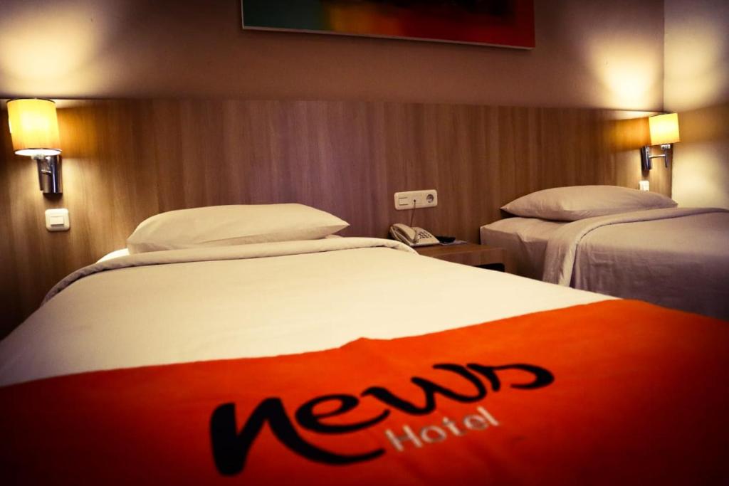 News Hotel Waru Sidoarjo في Waru: غرفة فندقية بسريرين عليها لافتة فندق جديدة