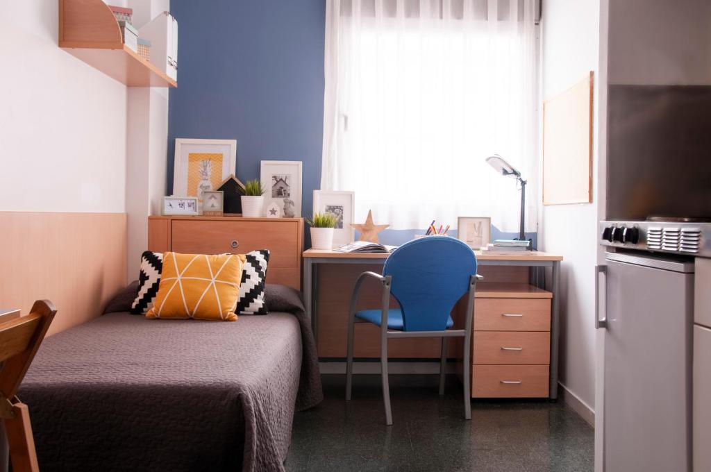 ein Schlafzimmer mit einem Bett und einem Schreibtisch mit einem blauen Stuhl in der Unterkunft Residencia Tomás Alfaro Fournier in Vitoria-Gasteiz