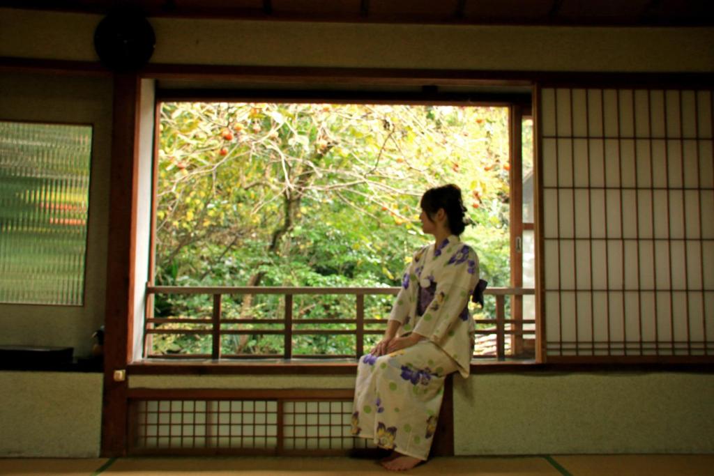 Una mujer en un kimono mirando por la ventana en Ougiya Ryokan, en Toyooka