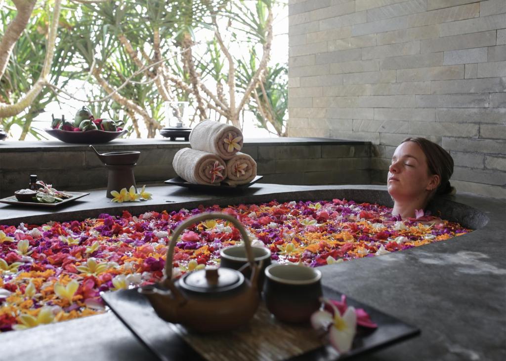 a woman laying in a bath tub covered in flowers at Kelapa Retreat & Spa in Pulukan