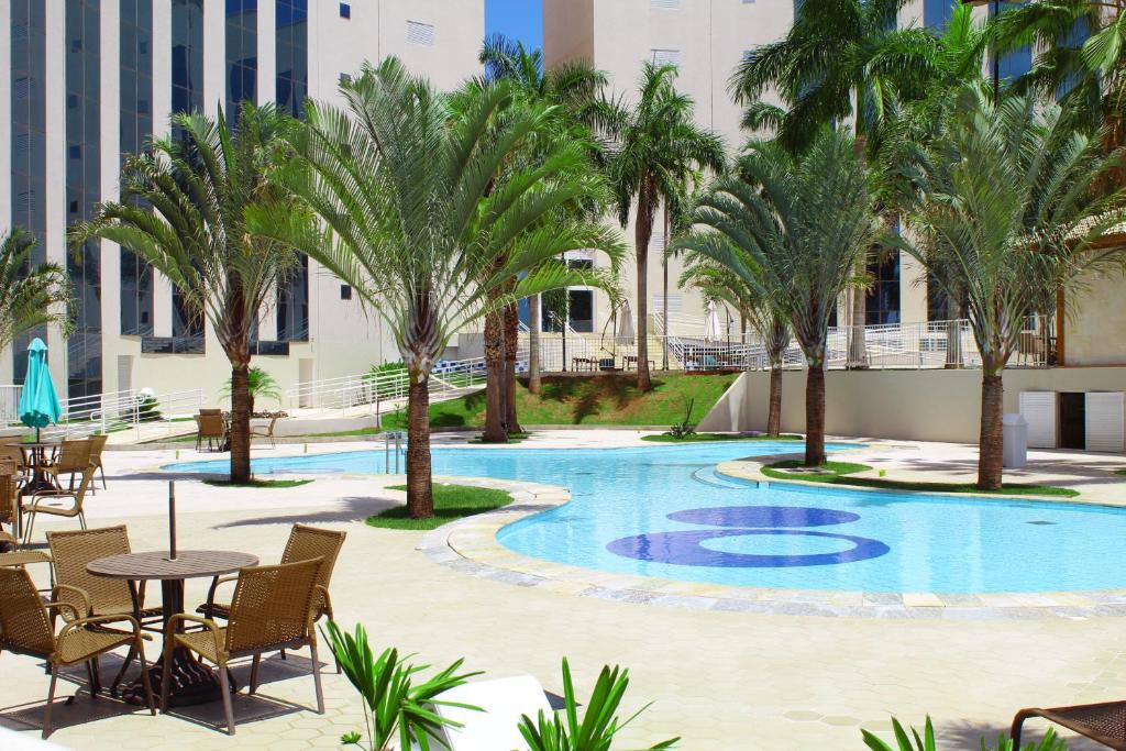 uma piscina com palmeiras, mesas e cadeiras em Barretos Park Hotel em Barretos