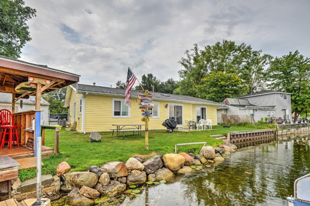 a yellow house with a flag next to a river at Lakefront Home Private Bar, BBQ, and Fire Pit! in Oxbow