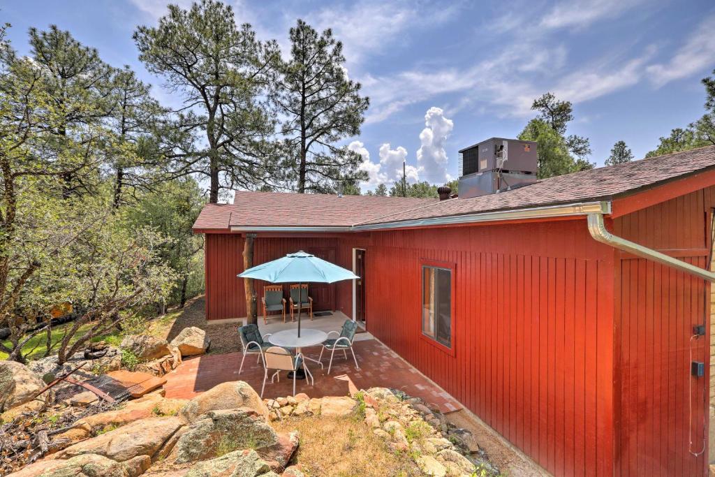 ein rotes Gebäude mit einem Tisch, Stühlen und einem Regenschirm in der Unterkunft Quiet Prescott Forest Retreat Cottage with Patio! in Prescott