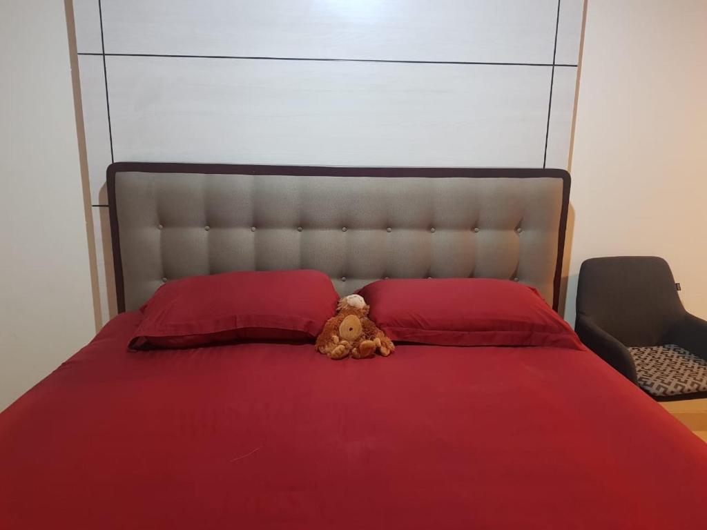 - un ours en peluche assis sur un lit avec des oreillers rouges dans l'établissement #7 Apartemen The Pinnacle - Louis Kienne Pandanaran Semarang, à Semarang