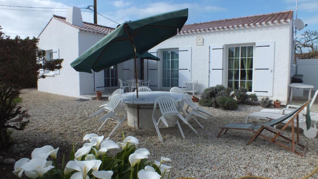um pátio com uma mesa e cadeiras e um guarda-sol verde em Noirmoutrine em Noirmoutier-en-l'lle