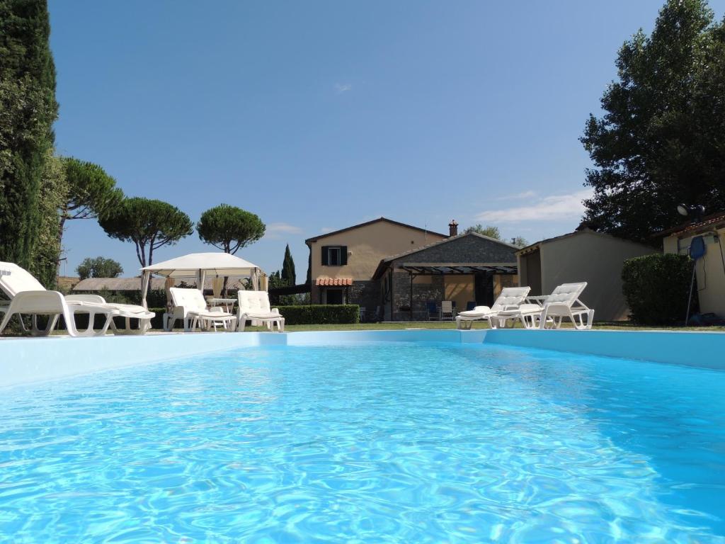 a large swimming pool with white chairs and a house at Podere Il Mulino in Pieve di Santa Luce