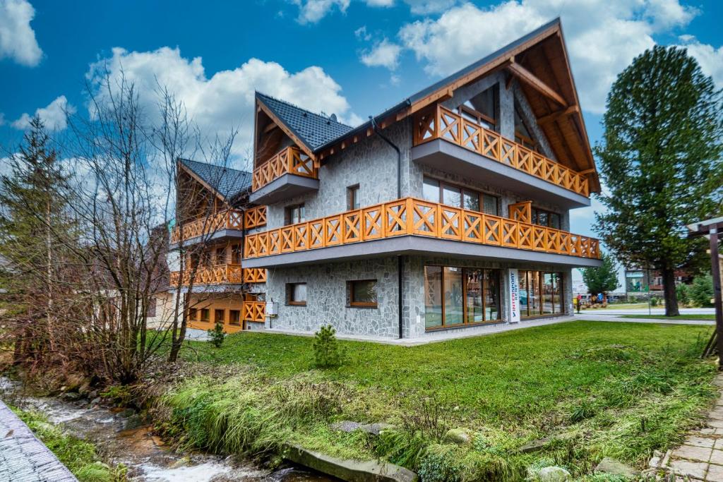 ein Haus mit Holzbalkonen auf einem grünen Hof in der Unterkunft Apartmán Alexander Tatranská Lomnica in Tatranská Lomnica