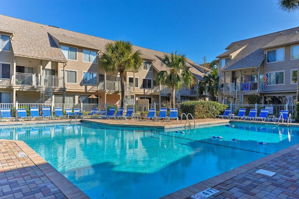 a swimming pool with blue chairs and condos at Hilton Head Villa with Balcony Walk to the Beach! in Hilton Head Island