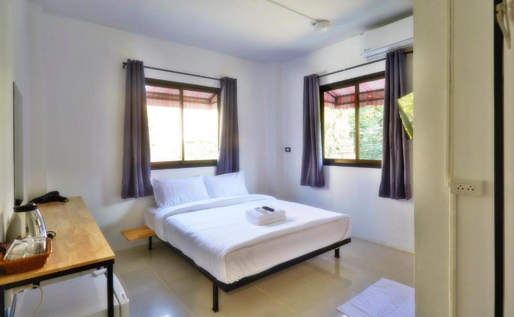 a bedroom with a white bed and two windows at GO INN Night Bazaar Chiang Mai in Chiang Mai