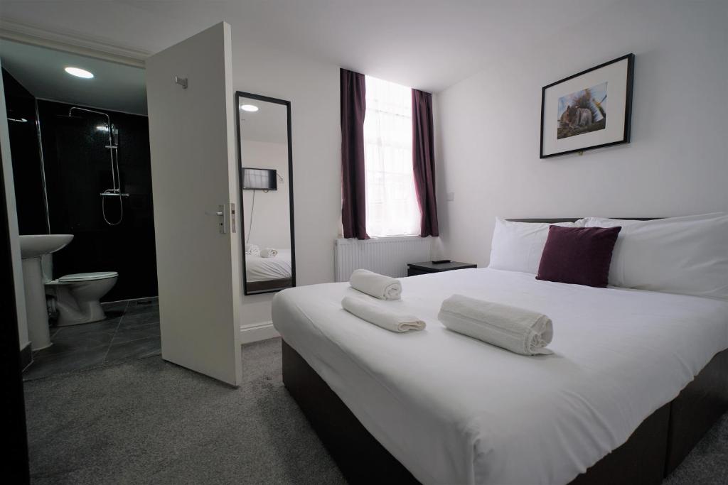 a bedroom with a large white bed and a bathroom at TBH Hotel in Barking