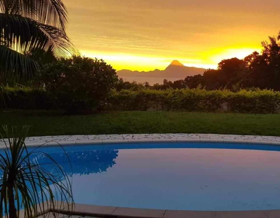 a sunset over a swimming pool with a mountain in the background at Le Tiki Rouge in Punaauia