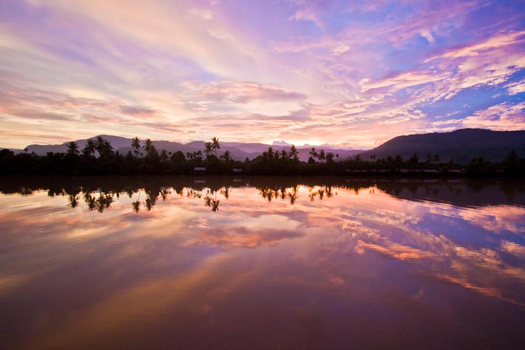 um pôr-do-sol sobre um lago com árvores e nuvens em Sabay Beach em Kampot