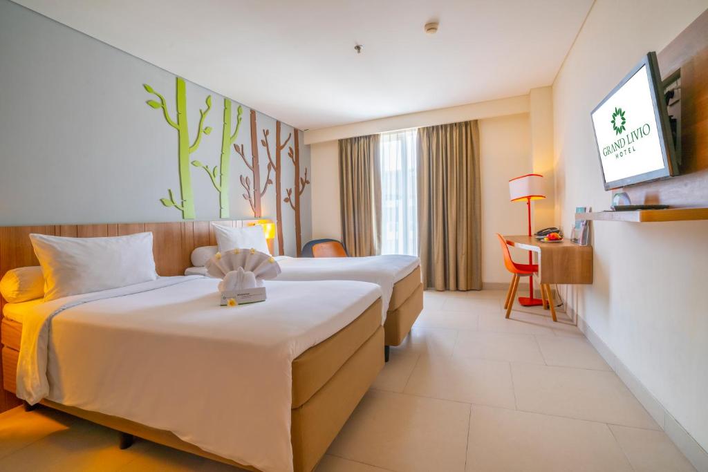 a hotel room with two beds and a television at Grand Livio Kuta Hotel in Legian
